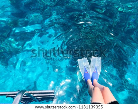 Beautiful female slender legs in diving fins for swimming are lowered into a blue marine transparent iridescent, luminous water on the sea, the ocean on a tropical cruise rest, a resort.