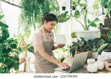 Beautiful Female Smiling Works At Garden Centre Retail Store. Taking Orders Over The Phone. She Working At Table And In Background Is A Shop With Lots Of Plant.