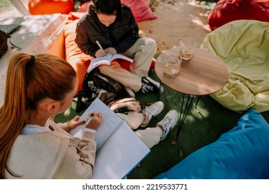 Beautiful Female Students Are Sitting On A Lazy Bags In A Coffee Bar, On A Beautiful Sunny Day And Studying Together For The Next Exam