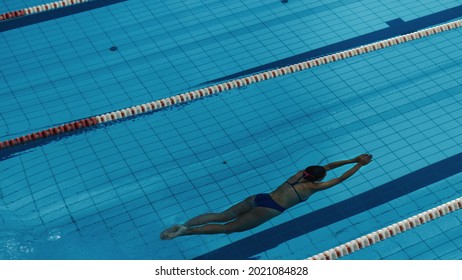 Beautiful Female Swimmer Diving In Swimming Pool. Professional Athlete Jumped From Starting Block, Swims Under Water. Person Determined To Win Championship. High Angle View.