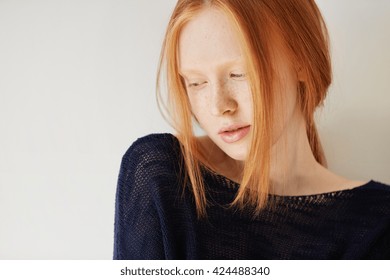 Beautiful Female Teenage Model Wearing Casual Black Top Looking Down With Shy And Thoughtful Expression On Her Face. Isolated Portrait Of Coy Redhead Student Girl With Freckles And No Make Up 