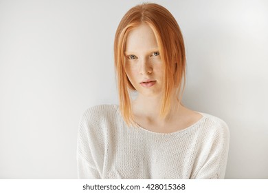 Beautiful Female Teenage Model Wearing Casual White Top Looking At The Camera With Thoughtful Expression On Her Face. Isolated Portrait Of Shy Redhead Student Girl With Freckles And No Make Up