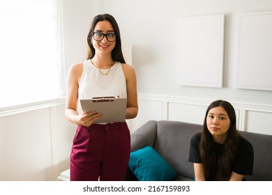 Beautiful Female Therapist Smiling And Looking At The Camera While Having A Therapy Session With A Sad Teen Girl 