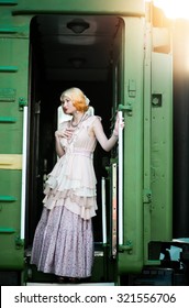 Beautiful feminine blonde girl in a vintage dress near the vintage train at the station - Shutterstock ID 321556706