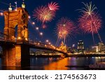 Beautiful fireworks fill the night time sky of Cincinnati Ohio as seen from Covington Kentucky across the Ohio River at night with the the John A Roebling Suspension Bridge