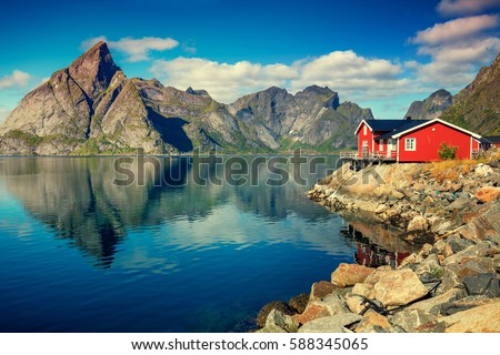 Beautiful fishing village on fjord. Beautiful nature with blue sky, reflection in water, rocky beach and fishing house (rorby). Lofoten, Reine, Norway