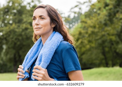 Beautiful Fit Mature Woman Resting After Workout. Proud Brunette Woman Relaxing With Blue Towel Around Neck After Yoga In Park. Thoughtful Mid Adult Woman Thinking After Sport And Looking Away.