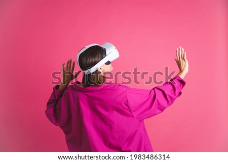 Beautiful fit tanned sporty woman in shirt in virtual reality glasses on pink background back ro camera