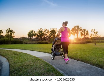 Beautiful, fit women walking and jogging outdoors along a paved sidewalk in a park pushing a stroller at sunset