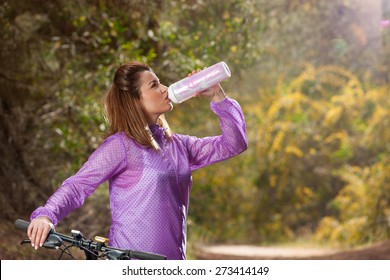 Beautiful fit young girl with bicycle drinking water in the nature - Shutterstock ID 273414149