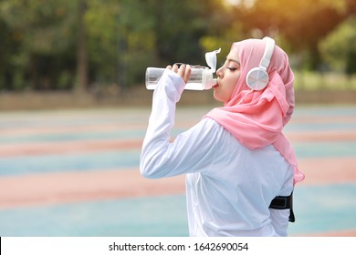 Beautiful fitness athlete asian muslim woman drinking water after work out exercising. Young cute girl standing in sportswear with headphone taking rest after workout outdoor.  Healthy, sport concept - Powered by Shutterstock