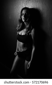 Beautiful Fitness Female - Side Lit Leaning Against A Dark Wall In Black Spandex Shorts And Top