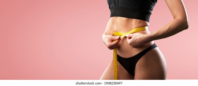 Beautiful fitness girl measuring her waistline with measure tape