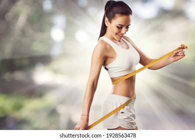 Beautiful fitness girl measuring her waistline with measure tape