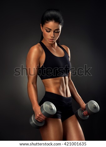 Beautiful fitness woman with  lifting dumbbells . Sporty girl showing her well trained body .  Well-developed muscles by strength training . 
