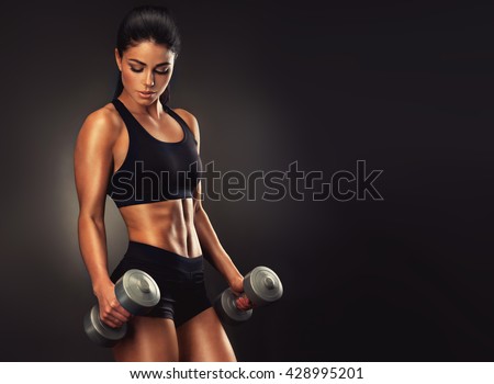 Beautiful fitness woman with  lifting dumbbells . Sporty girl showing her well trained body .  Well-developed muscles by strength training . 