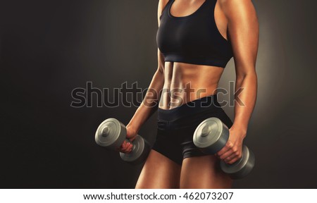 Beautiful fitness woman with  lifting dumbbells . Sporty girl showing her well trained body .  Well-developed muscles by strength training . 