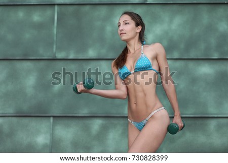 Beautiful fitness woman lifting dumbbells Sports on the street