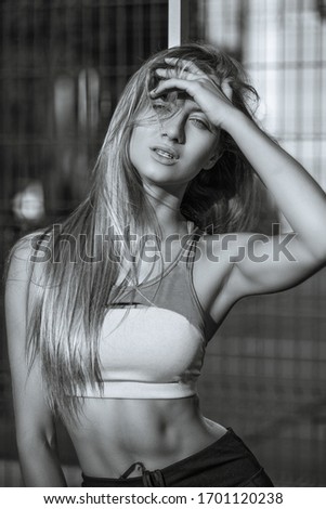 Beautiful fitness woman with perfect body wearing sport clothes posing on a tennis court in rays of sun. Black and white color