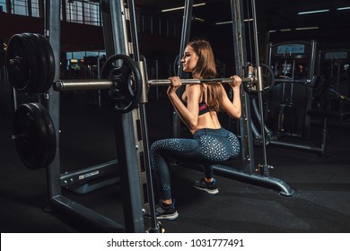 Beautiful Fitness Young Girls Doing Squats With The Barbell In Smith Machine At The Gym. Perfect Fitness Female Figure