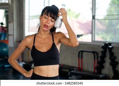 Beautiful Fitness Young Woman Tired Taking A Break From Exercise Cooling Down From Water Bottle Touching Her Face In Gym . Healthy Sport Girl In Sportswear Workout .