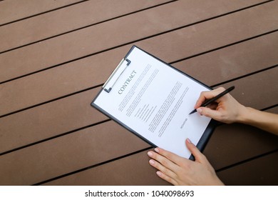 beautiful flat lay of young woman hands with pen sign contract, wooden backgroung. concept of business work agreement, freelance working remotely. Front used with Open Font License