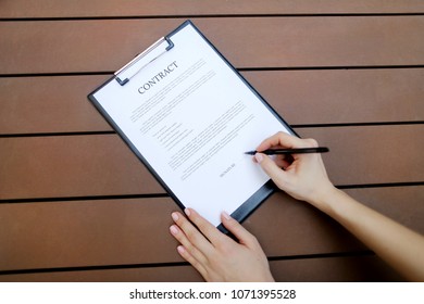 beautiful flat lay of young woman hands with pen sign contract, wooden backgroung. concept of business work agreement, freelance working remotely. Front used with Open Font License
