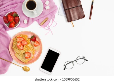 Beautiful flatlay arrangement with cup of coffee, hot waffles with cream and strawberries, glasses and other business accessories: concept of busy morning breakfast, white background.