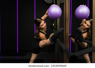 Beautiful flexbile woman doing stretching exercises in front of the mirror at the fitness center doing barre exercises - Powered by Shutterstock