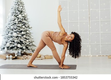 Beautiful flexible young woman is doing stretching exercise near decorated fashion christmas tree