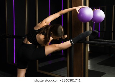 Beautiful flexible young woman stretching using a fitness ball seen from behind while exercising at a barre class at the gym - Powered by Shutterstock