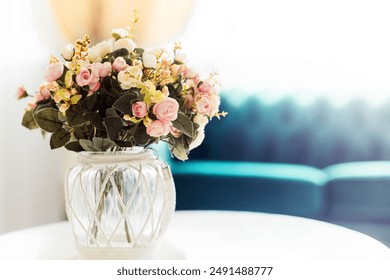 A beautiful floral arrangement in a glass vase with a white rope accent, placed on a white table in a cozy living room. - Powered by Shutterstock