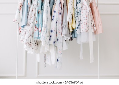 Beautiful Floral Dresses For Girls On Hangers At The Background Of White Wall. Kids Dresses For Prom And Holiday. 