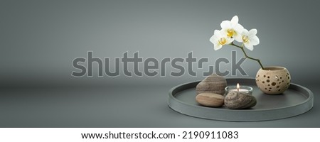 beautiful floral home decoration composition with white orchid and candle on grey pure background, lifestyle concept with copy space for product presentation