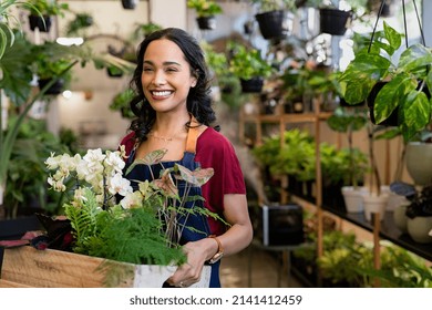 Beautiful florist holding wooden box of fresh plants at flower shop. Latin hispanic woman working in floral shop with copy space. Successful florist smiling while holding fresh flowers and plants.