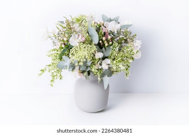 Beautiful flower arrangement of delicate pink flowers, Eucalyptus leaves, Queen Anne's Lace, and lush green foliage, in a grey vase, with a white background. - Shutterstock ID 2264380481