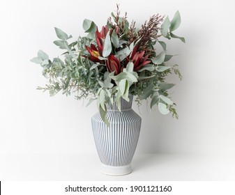 Beautiful Flower Arrangement Of Mostly Australian Native Flowers, Including, Silvan Reds, Wattle Foliage And Eucalyptus Leaves, In A White And Blue Strip Vase, With A White Background.