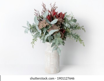 Beautiful flower arrangement of mostly Australian native flowers, including Silvan Reds, Queen Anne's Lace, Wattle foliage and Eucalyptus leaves, in a ceramic white vase, with a white background. - Shutterstock ID 1901127646