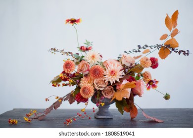 Beautiful flower composition with autumn orange and red flowers and berries. Autumn bouquet in vintage vase on a white wall background - Shutterstock ID 1808519041