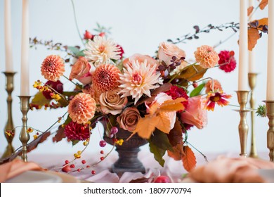 Beautiful flower composition with autumn orange and red flowers and berries. Autumn bouquet in vintage vase on a wooden table with pink tissue and candles