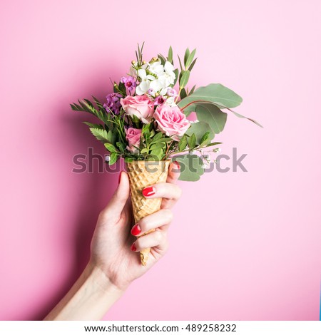 Beautiful flower in ice cream cone in girls hand with manicure on pink background
