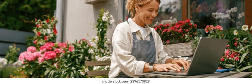 Beautiful flower shop owner wearing apron working on laptop in her store - Powered by Shutterstock