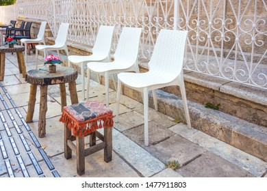A beautiful flower stands on a table made of wood cut. Next to the wooden table is a small wooden chair and several white plastic chairs. A cozy place to relax on the street of the beautiful city. - Shutterstock ID 1477911803