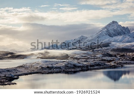 Beautiful foggy moutain and snow landscape in Lofoten Islands archipelago in Northern Norway with a church hidden in the fog, frozen sea, water reflection
