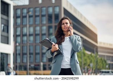 Beautiful Formal Dressed Business Woman In Suit With A Laptop And Notebook Outdoor. Brunette Caucasian Female, Standing Near Office.