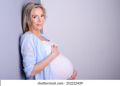 Beautiful Forty Years Old Pregnant Woman With Blue Shirt Isolated On A Gray Background