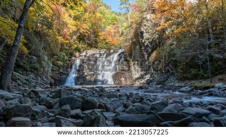 Beautiful forty-foot tall, fifty-foot-wide waterfall framed by colorful autumn foliage and river stones.