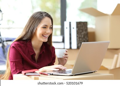 Beautiful freelance worker working on line with a laptop during office relocation with carton boxes in the background