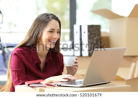 Beautiful freelance worker working on line with a laptop during office relocation with carton boxes in the background