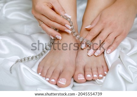 Beautiful French pedicure and manicure in pink and white with rhinestones for the bride. Toes and hands close up. Wedding accessories.